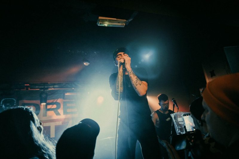 Adam Rossi from Glass Heart on stage holding a microphone with both hands while surrounded by the crowd