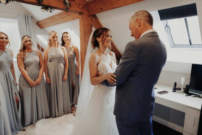 Proud father of the bride seeing his daughter's wedding dress for the first time, sharing a hug