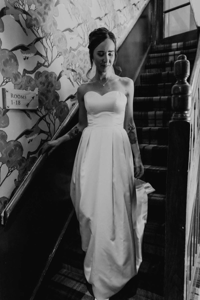 Black and white shot of bride coming down the stairs smiling