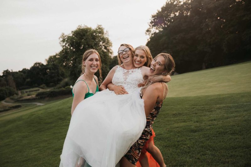 Bride helplessly being lifted into the air by her bridesmaids and friends