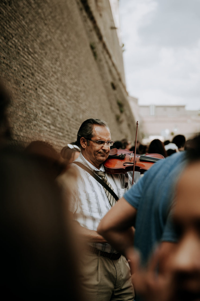 Personal work. Man playing the violin in the middle of a busy street in Rome, surrounded by people.