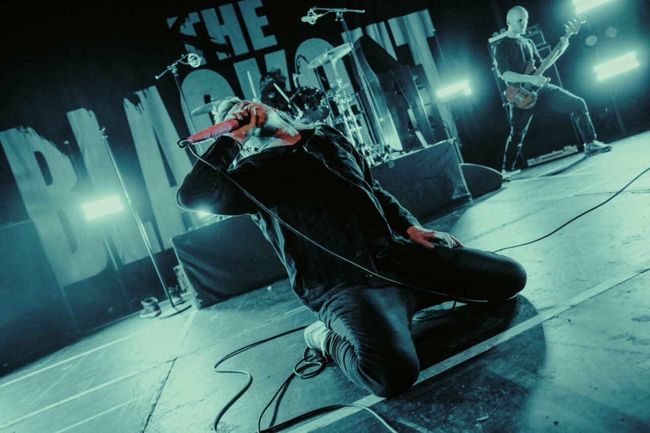 Sean Smith of The Blackout knelt on stage screaming into a mic in Cardiff Great Hall. Shot on the Blackout Reunion tour, Feb 2024.