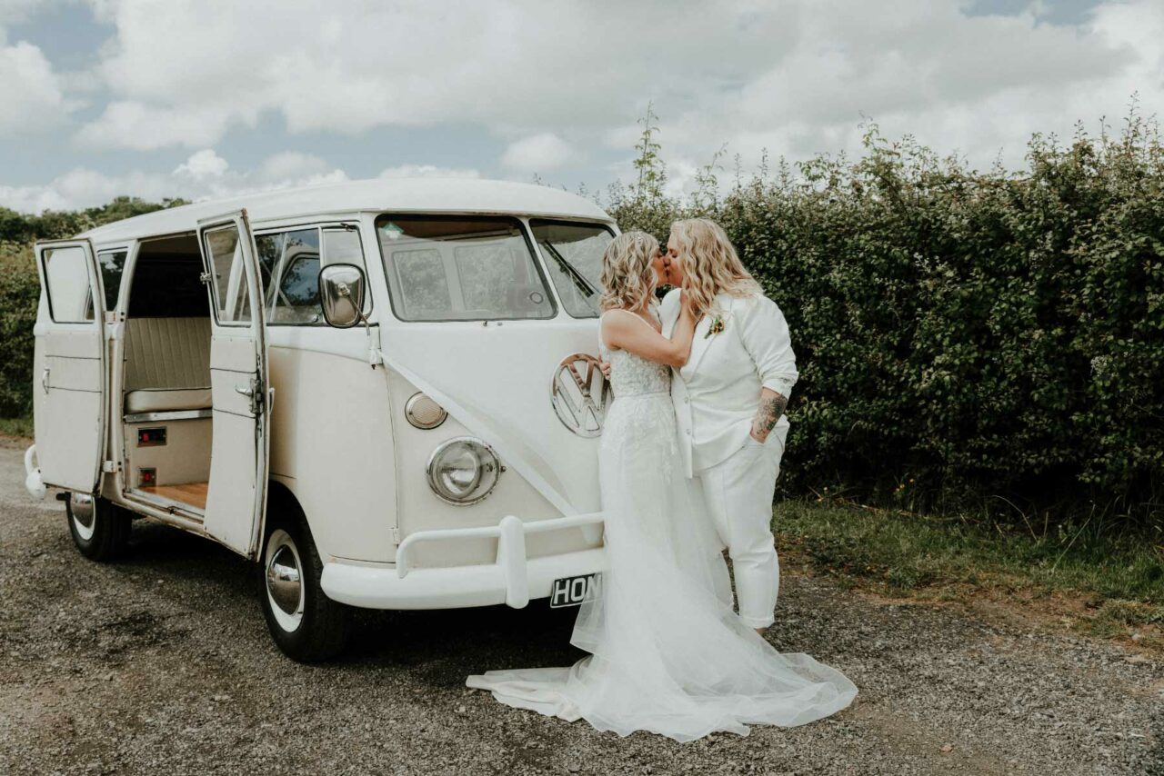 Two happy, newly wed women sharing a kiss in front of a VW camper van. Shot at Dyffryn Springs wedding venue, June 2024.