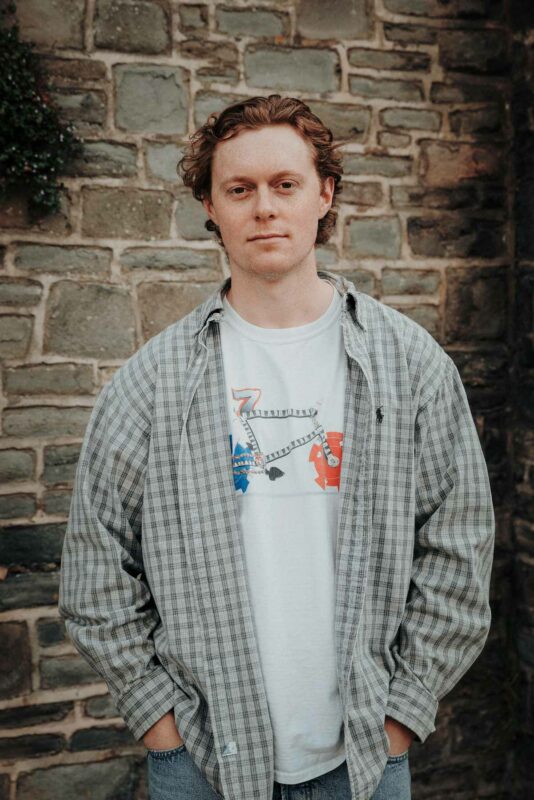 Portrait of a man with his hands in pockets, staring at the camera.