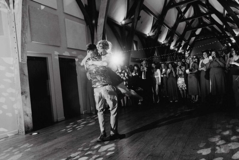 Black and white shot of a happy couple during their first dance, surrounded by their friends and family.