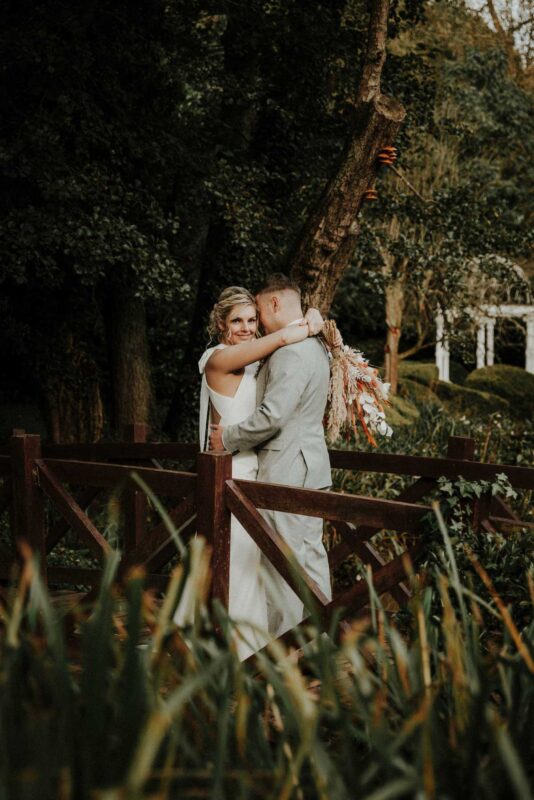 Portrait of a happy couple stood romantically on a bridge on their wedding day. Shot at the Mill Barns wedding venue.