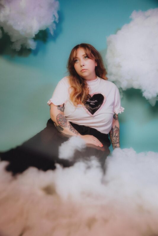 The singer of indie pop band Parcs sat against a blue backdrop, surrounded buy self built pink fluffy clouds. Shot as part of a press shoot at Citrus Studio, Cardiff.