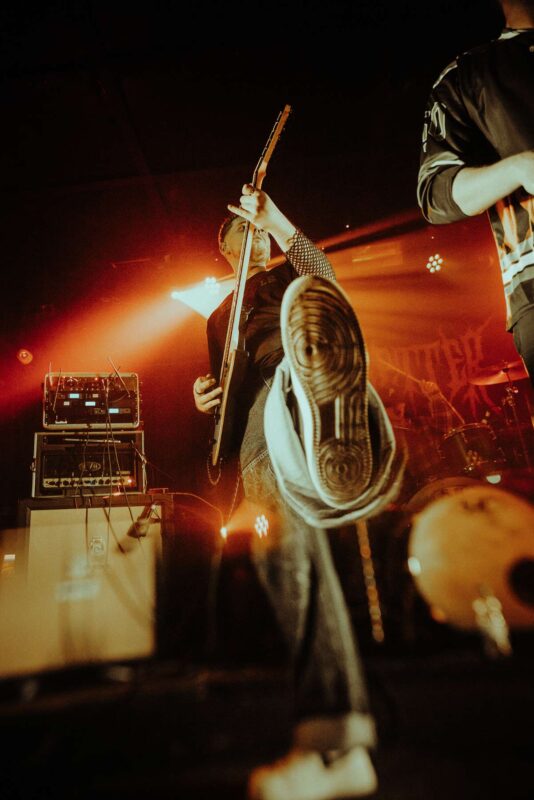 Swindon deathcore band BreakFifty's guitarist on stage in the Bunkhouse Swansea, kicking his foot towards the camera.