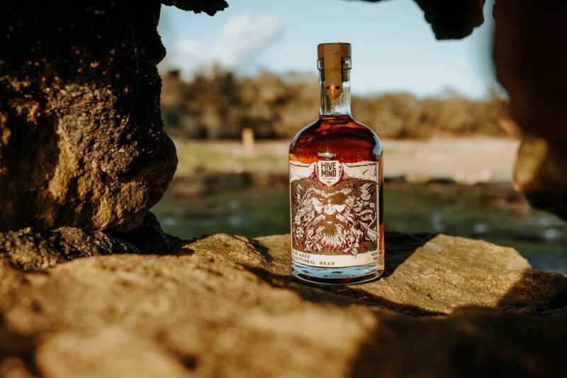 Promotional product image of a bottle of Hive Mind rum aged mead set in a coastal, shipwrecked styled setting. Shot as part of a promotional marketing shoot, Nov 2024.