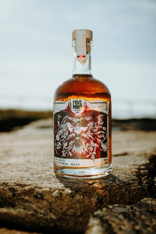 Promotional product image of a bottle of Hive Mind rum aged mead set in a coastal, shipwrecked styled setting. Shot as part of a promotional marketing shoot, Nov 2024.