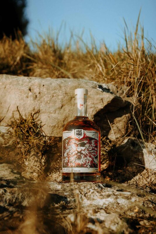 Promotional product image of a bottle of Hive Mind rum aged mead set in a coastal, shipwrecked styled setting. Shot as part of a promotional marketing shoot, Nov 2024.